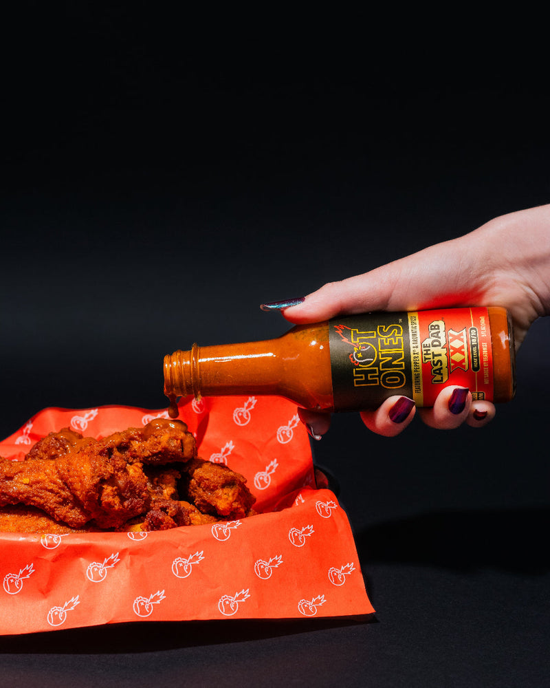 Hand pouring hot sauce over fried chicken on a black background